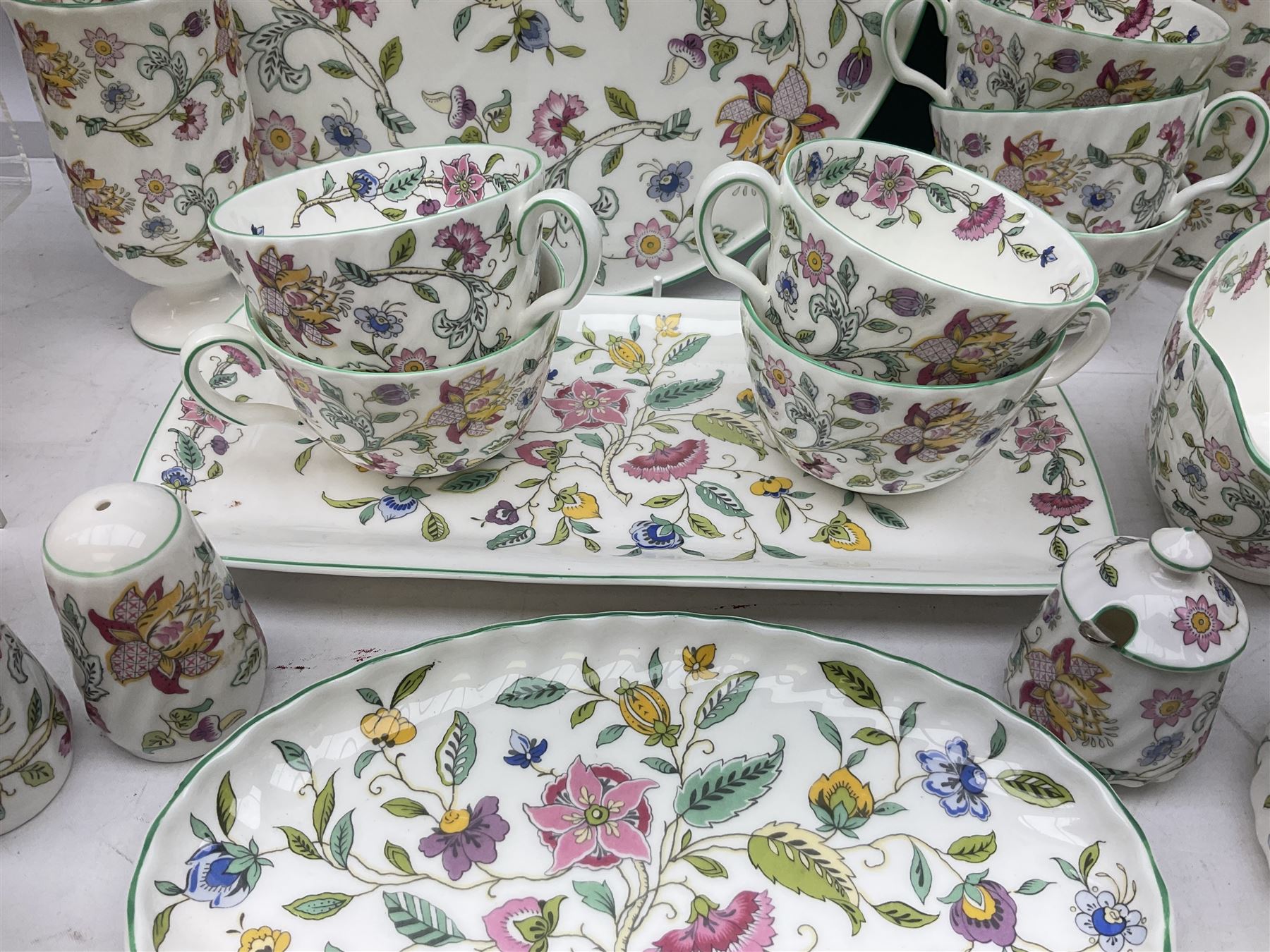 Minton Haddon Hall pattern tea and dinner wares, including basket dish, two covered tureens, six dinner plates, eight dessert plates, twelve tea plates, six soup bowls, six cereal bowls, teapot, coffee pot, milk jug, covered sucrier twelve tea cups and saucers, six mugs, footed bon bon dish, pair of candlestick holders, cake knife and slice etc (81)