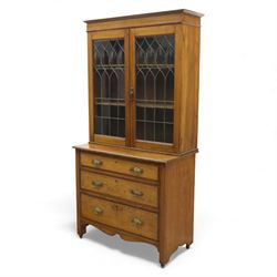 20th century wooden bookcase cabinet, fitted with a pair of leaded glass panel doors opening to adjustable shelves, the base top and front veneered in richly figured walnut, contrasted with solid oak panelled sides and shaped lower frieze, terminating in castors