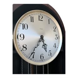 English- Art deco mahogany 8-day longcase clock, with an arched top and fill length fully glazed door beneath, on a short plinth with bracket feet, three train chain driven movement with visible stainless steel cased weights and pendulum, silvered dial with Arabic numerals, minute track and pierced steel hands, quarter chiming movement with  Westminster/ Whittington/ strike/silent selection.
