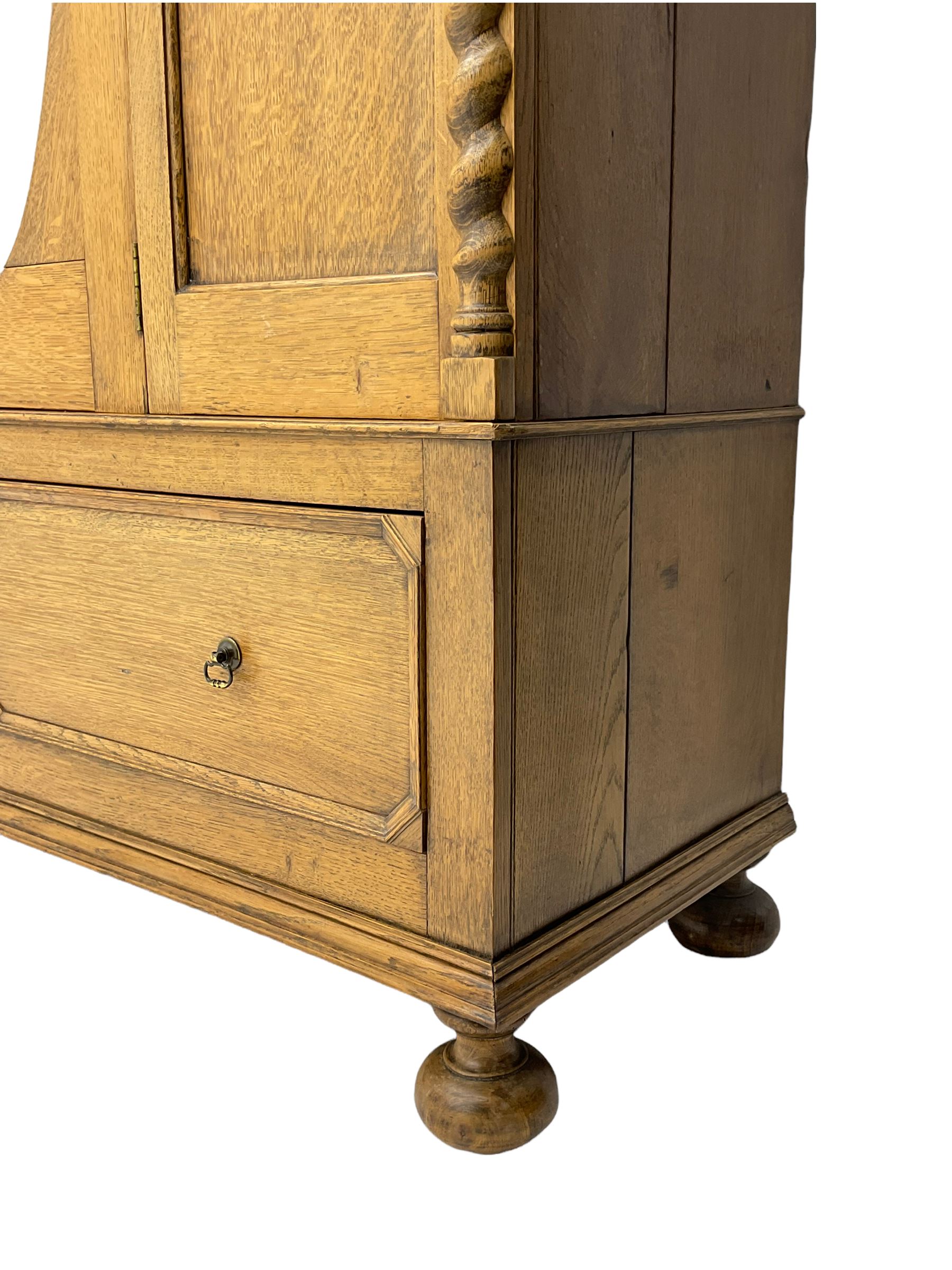 Early 20th century oak wardrobe, projecting cornice of blind fret-work frieze, oval bevel edge mirror door, half spiral turned pilasters, drawer to base with mouldings, on turned bun feet