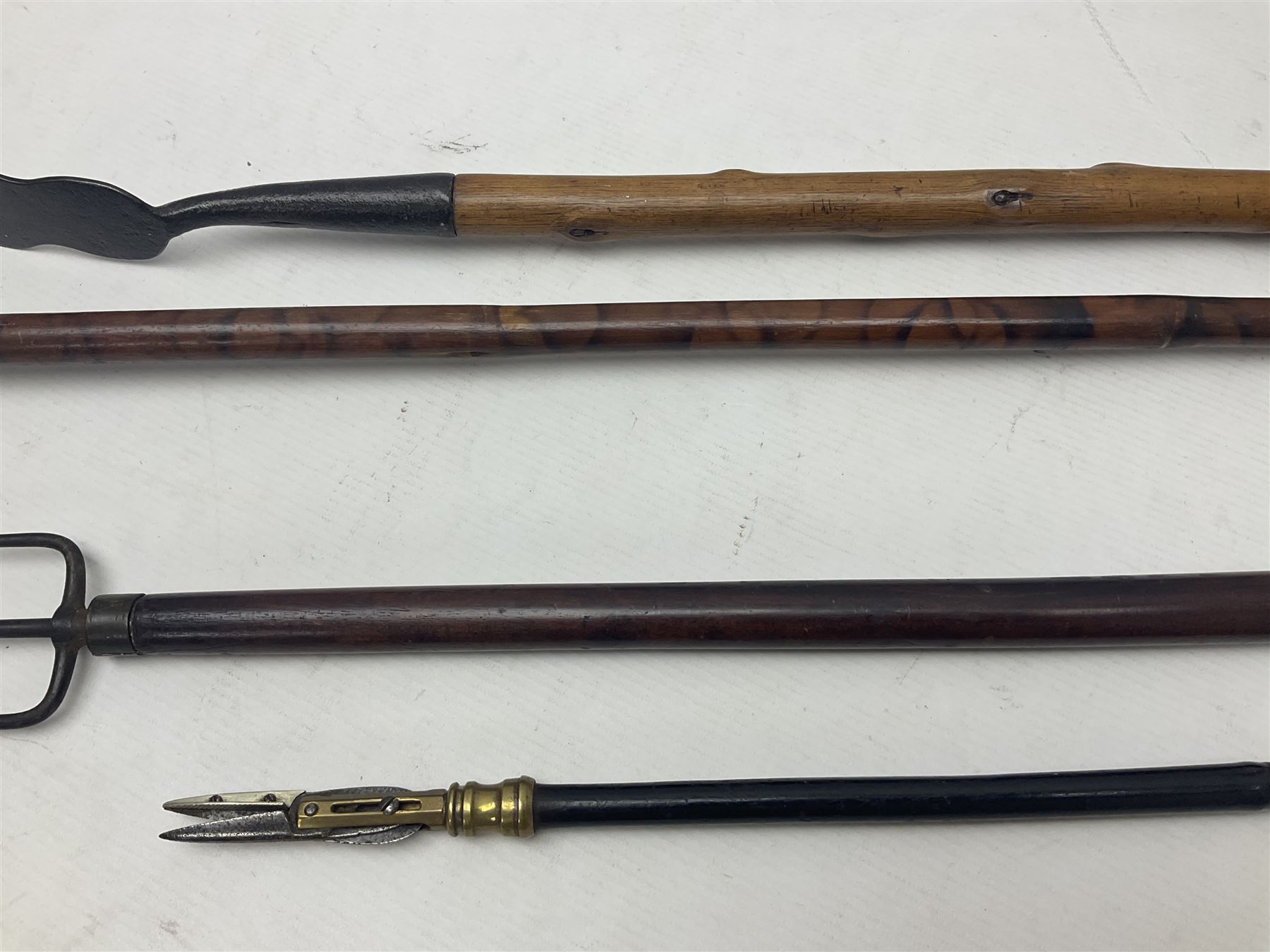 Two late 19th century fruit picker canes, the first example a French ebonised bamboo cane, with pair of fruit scissors to base, the handle stamped Cueille Fruit, the second example with grabbing action, the cap stamped A C Harris, Leicester, together with two other 19th century canes, one with fork and the other with hoe