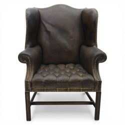Georgian style leather wing armchair, shaped high back with outscrolled wings above padded arms and deep buttoned seat, close-nailed throughout, raised on square supports united by H-stretcher
