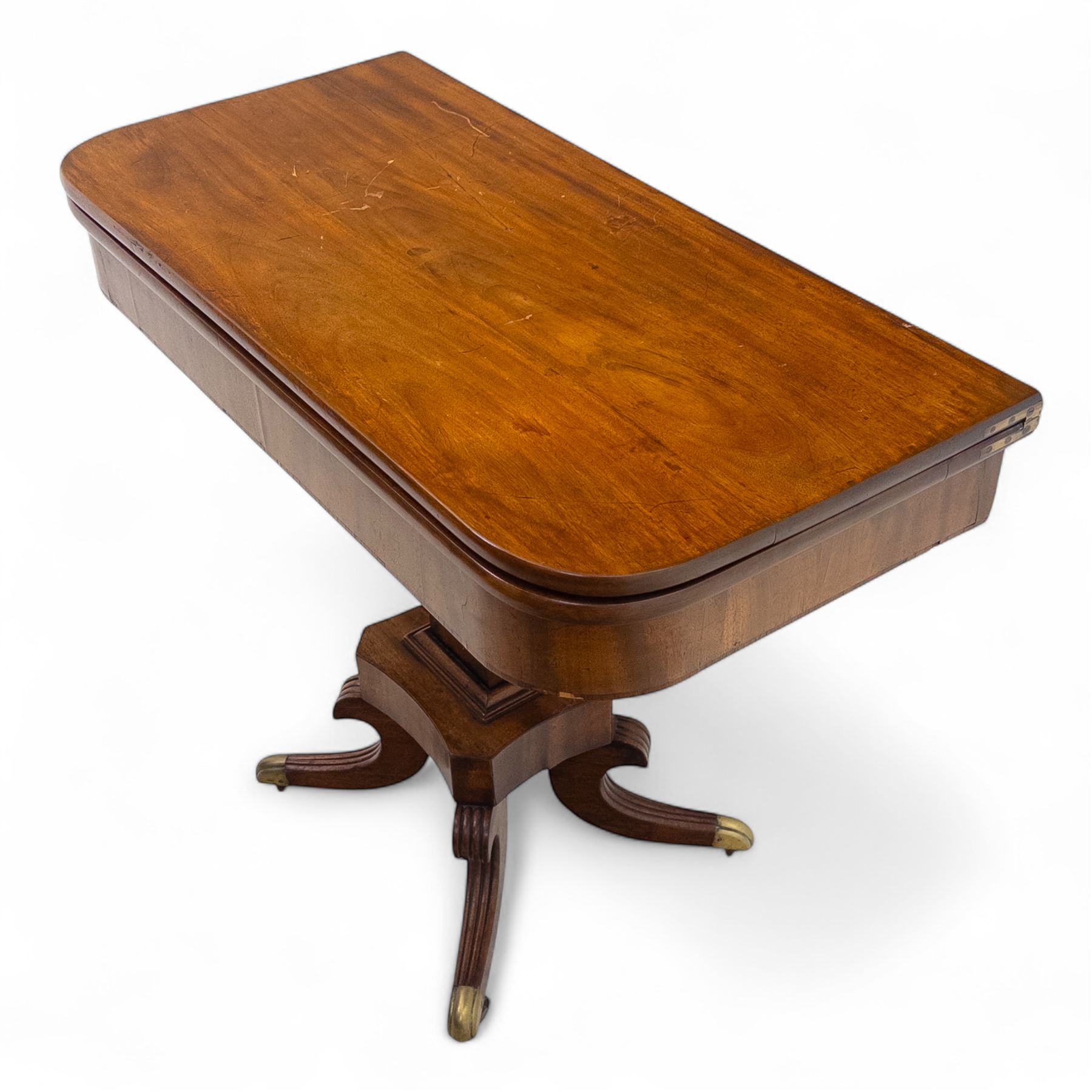 Regency mahogany fold-over table, hinged top with rounded corners opening to reveal a plain polished surface, supported on moulded pedestal base with reeded downswept legs, terminating in brass cups and castors (Extends to 90cm)