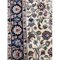 North East Persian Meshed hand-knotted rug, ivory field with scrolling vines, palmettes, and rosettes in shades of blue and brown, within a dark blue border of palmettes and flowerheads between multiple guard stripes, with cotton fringe ends  