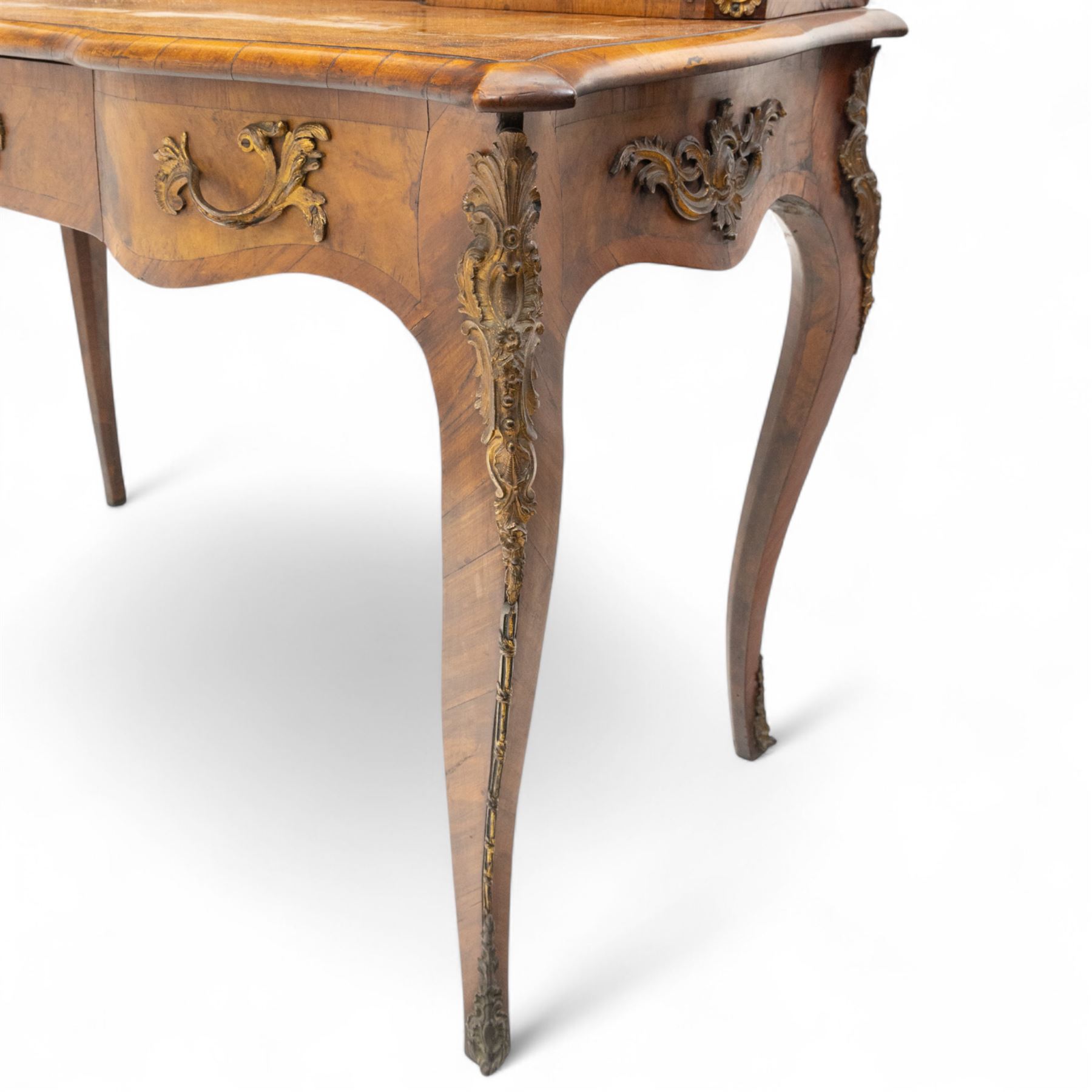 Late 19th-century Louis XV revival gilt bronze mounted and walnut Bonheur-de-Jour, rectangular-shaped serpentine form, with gilt bronze beading, frieze with two blind drawers and gilt bronze handles, centre drawer with large central serves style porcelain plaque, the elevated section with brass gallery above panelled cupboard doors also with serves style porcelain plaques and gilt bronze mounts, interior with single shelf, central section with four drawers each with gilt bronze handles, raised on slender cabriole legs fitted with gilt bronze rococo style masks and sabots