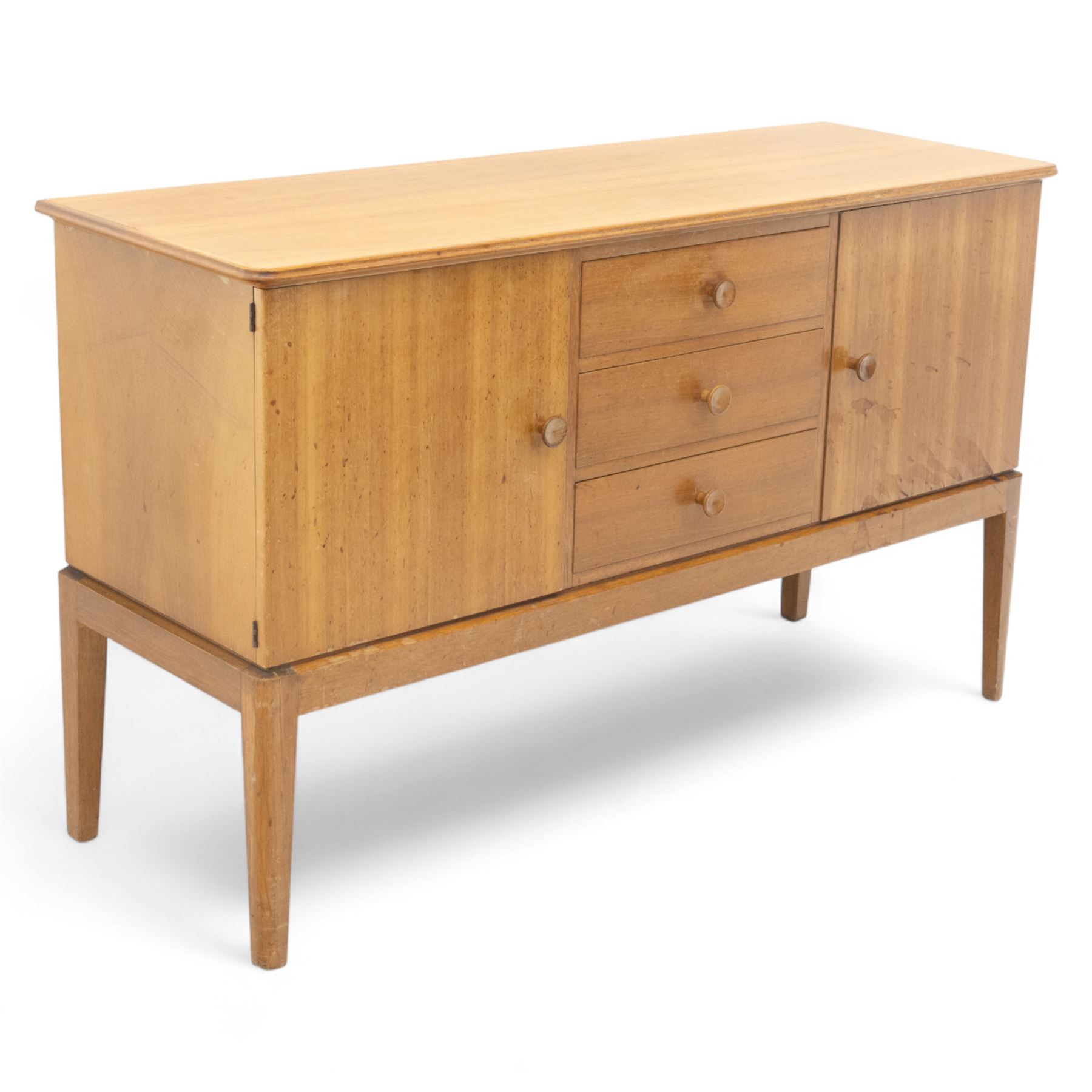 Gordon Russell - mid century modern teak sideboard, the rectangular top with rounded edges over twin cupboards and three central drawers, fitted with circular wooden pulls, on tapered supports, reflecting the firm’s commitment to simplicity and quality materials during the post-war design period