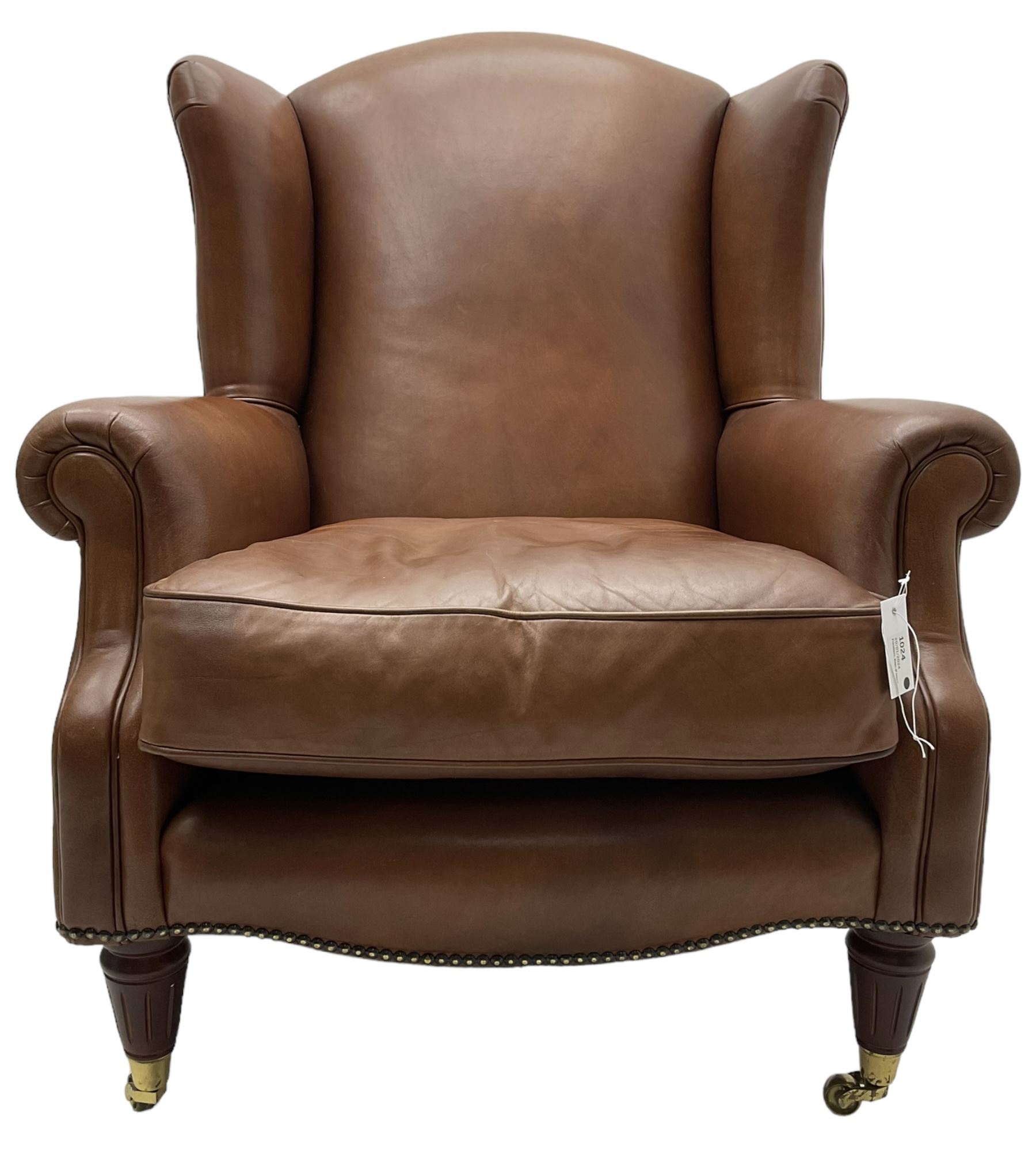 Georgian design wingback armchair, upholstered in brown leather with stud band and piping, turned and fluted front feet on brass cups and castors