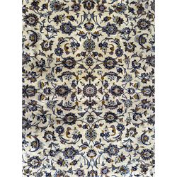 Central Persian Kashan hand-knotted carpet, ivory field with an all-over design of scrolling vines, lotus palmettes, and rosettes in shades of blue, gold, and brown within a blue ground border of palmettes and arabesques between multiple guard stripes