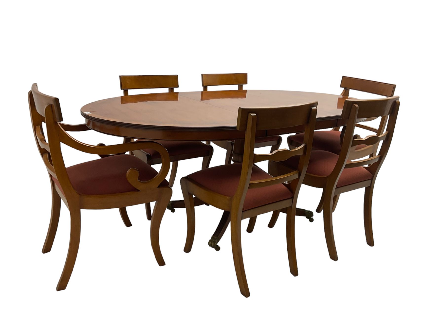 Regency design yew wood dining table, oval cross-banded top with reeded edge, raised on turned pedestal with reeded sabre supports terminating in brass hairy paw feet and castors (W138cm D100cm H75cm); and Rackstraw - set six (4+2) Regency design dining chairs with red drop-in seats (W50cm H86cm)