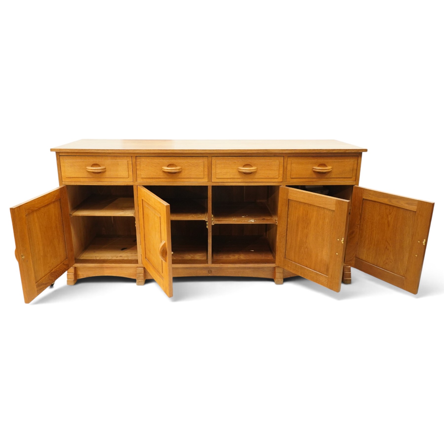 Acorn Industries - oak dresser base or sideboard, the rectangular top over three drawers with protruding oak handles, over four panelled cupboard doors enclosing a single shelf, raised on stepped feet, carved with acorn signature, by Alan Grainger, Brandsby