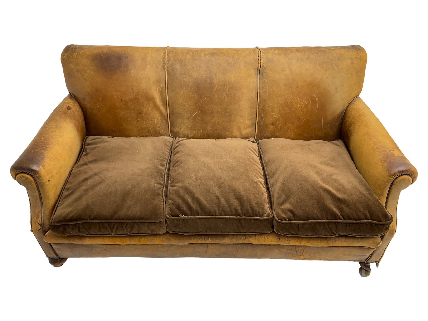 Early-to-mid-20th century three seat sofa, upholstered in worn tan leather with studwork, loose cushions upholstered in brown fabric, on compressed bun feet with castors