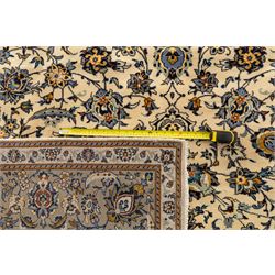 Central Persian Kashan hand-knotted rug, ivory field intricately decorated with an all-over design of scrolling vines, palmettes, and stylized lotus motifs in shades of soft blue, pale gold, and indigo within floral borders