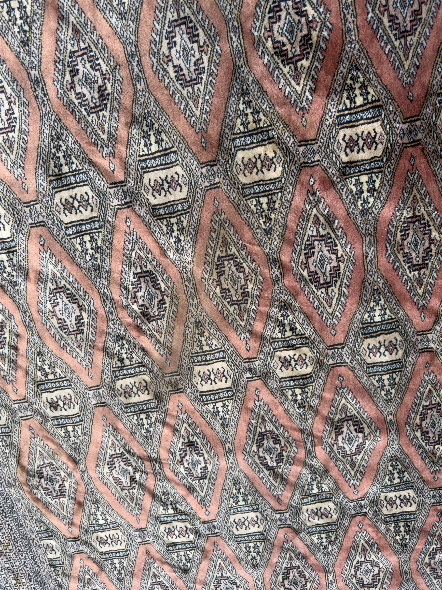 Large Persian Bokhara wool rug, the field decorated with repeating gul motifs in lozenge medallions across a dark ground, enclosed by multiple geometric borders in indigo, ivory and terracotta, from the region of Baluchistan