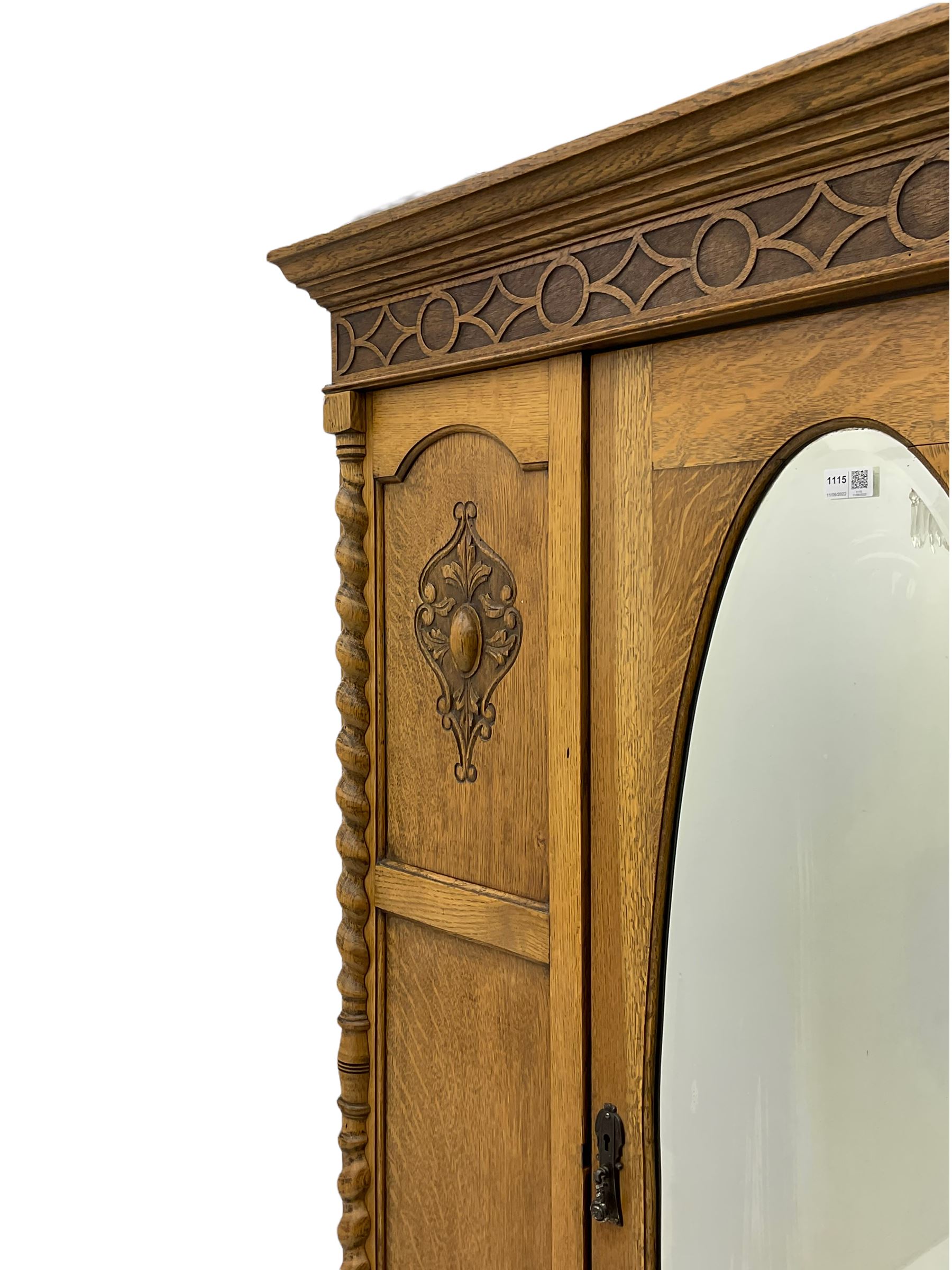 Early 20th century oak wardrobe, projecting cornice of blind fret-work frieze, oval bevel edge mirror door, half spiral turned pilasters, drawer to base with mouldings, on turned bun feet