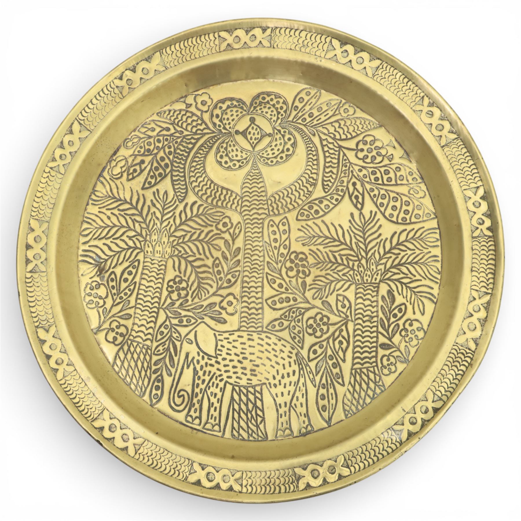 20th century Eastern brass charger topped table, the circular brass trap chased with an elephant, palm tress and flowering vines, supported upon a folding stand with six turned legs with inlaid detail, united by turned supports