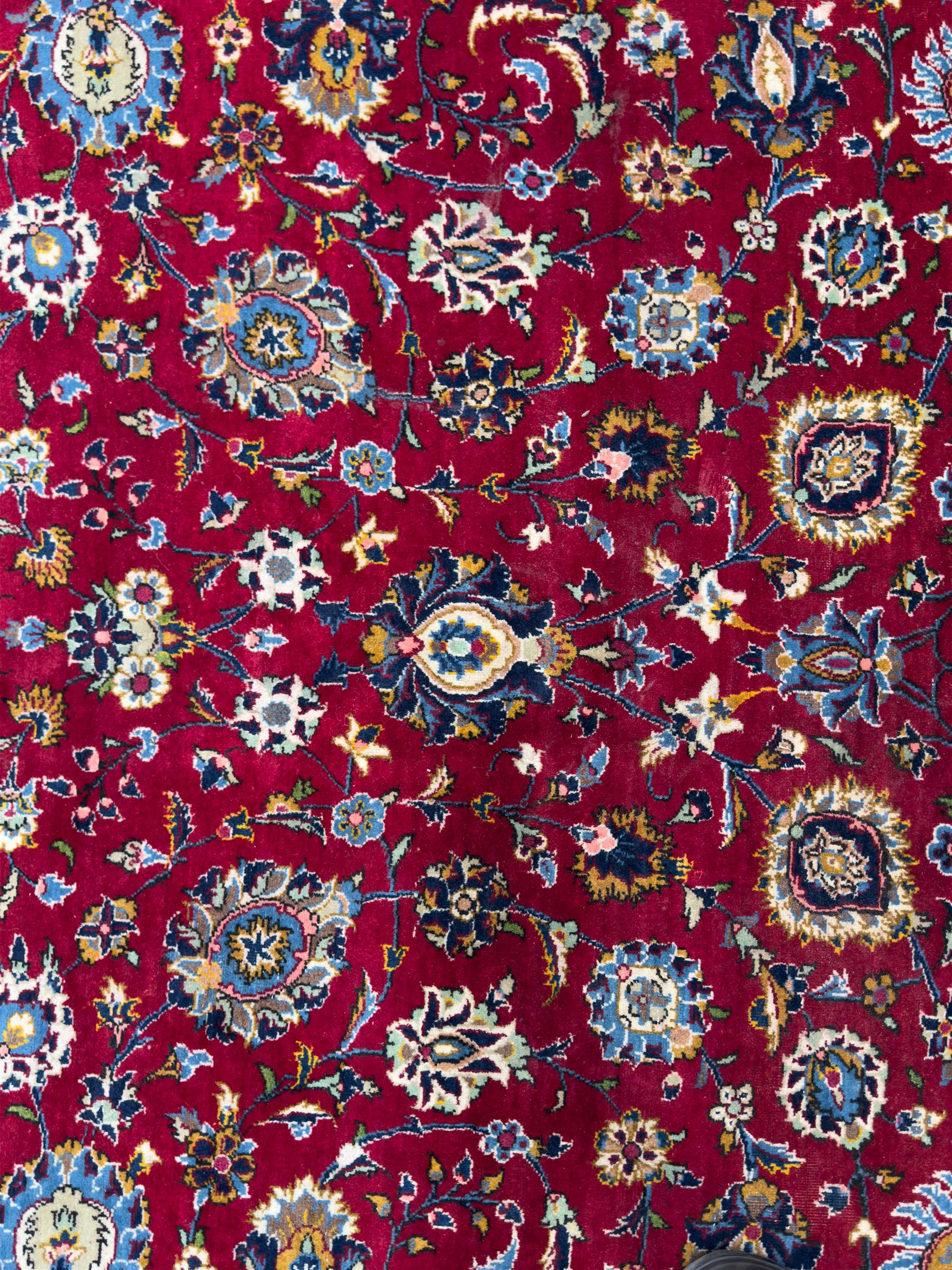 Northeastern Persian Meshed hand-knotted carpet, madder red field with an all-over design of scrolling vines, palmettes, and rosettes, within a dark blue border of palmettes and arabesques 