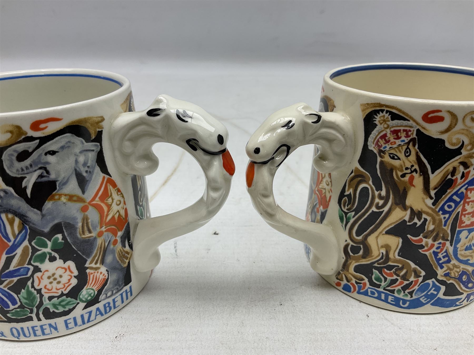 Two Dame Laura Knight coronation mugs for King George VI and Queen Elizabeth, comprising a Burleigh Ware example and a J&G Meakin example, each with a lion moulded handle and printed marks beneath, H8cm