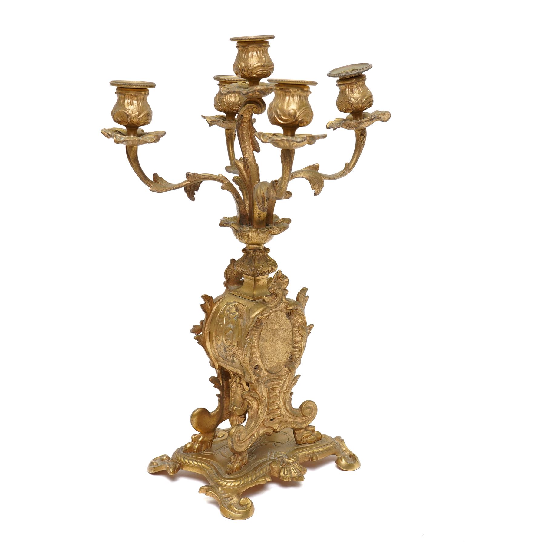 French-Late 19th century 8-day gilt brass rococo style mantel clock, c1890, waisted case  decorated with scroll work, leaves and musical instruments, resting on an attached plinth with splayed feet, dial within a glazed brass bezel with a gilt repoussé centre, porcelain cartouche Roman numerals and steel fleur-di-Lis hands, with a twin train movement, recoil anchor escapement and countwheel strike, sounding the hours and half-hours on a bell. With a matching pair of five-light candelabra. No Pendulum or Key.