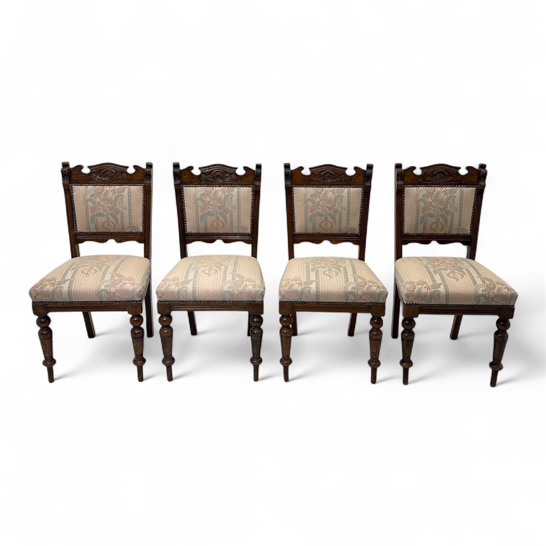 Victorian walnut set of four dining chairs, the shaped and carved top rails with central flowerhead and scroll decoration above upholstered backs and seats in floral woven fabric, brass stud trim, on ring turned front supports