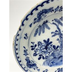 Three English Delftware plates, each decorated with a Chinese inspired scene with peonies, fir trees, and fence, smallest example with ochre rim line indistinctly signed beneath, largest D22.5cm, smallest D19.5cm