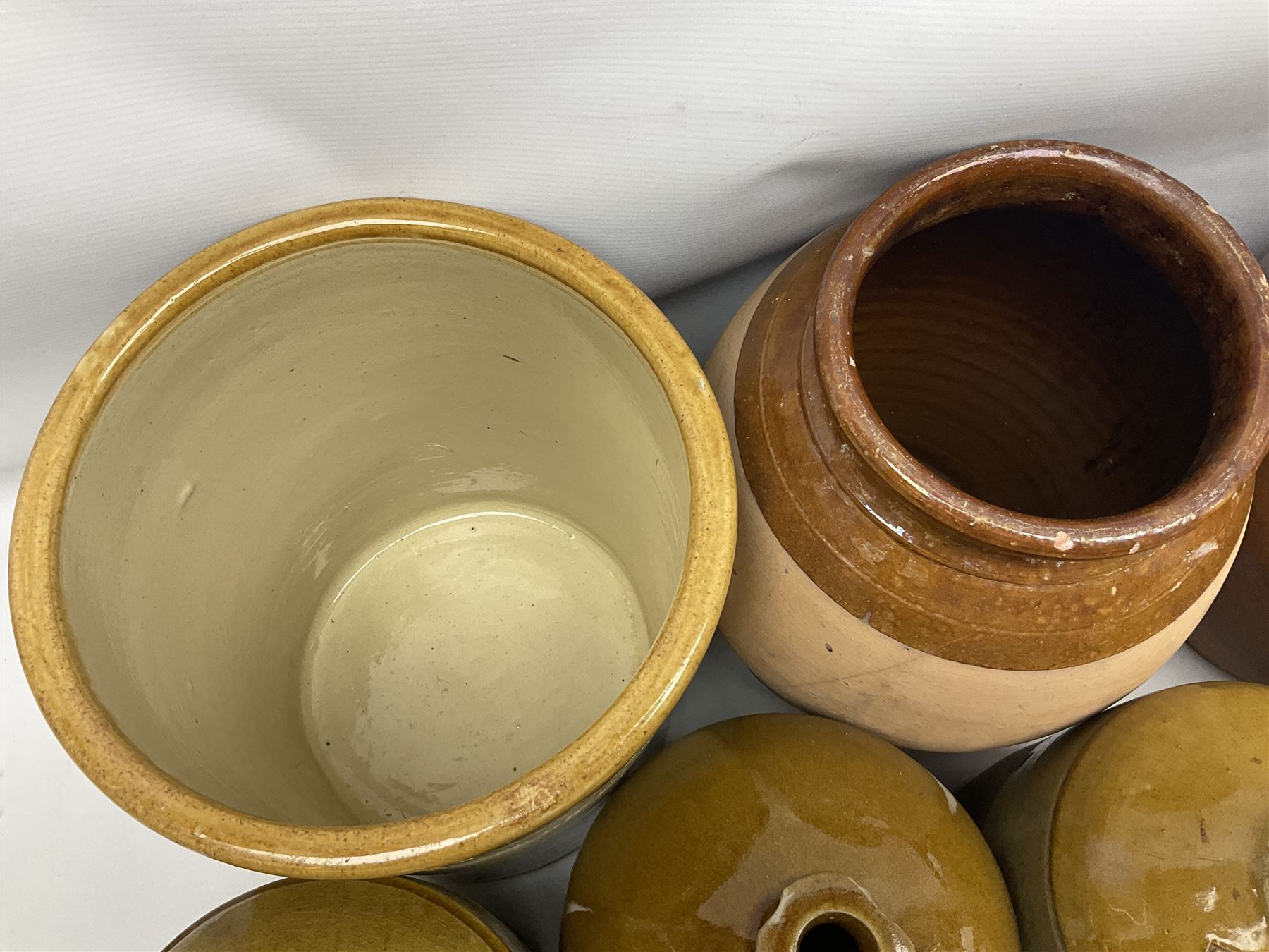 Quantity of stoneware flagons, to include Skipton, Clitheroe and Hellifield related examples, four salt glazed bottles, large cylindrical stoneware jar, large twin handled jar and vase, together with two brass jam pans, tallest H35cm