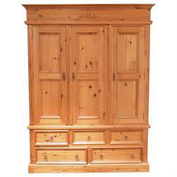 20th century pine wardrobe with drawer base, moulded cornice over three fielded panel cupboard doors enclosing hanging compartments, the base fitted with three short and two long drawers with brass ring handles, raised on a plinth base