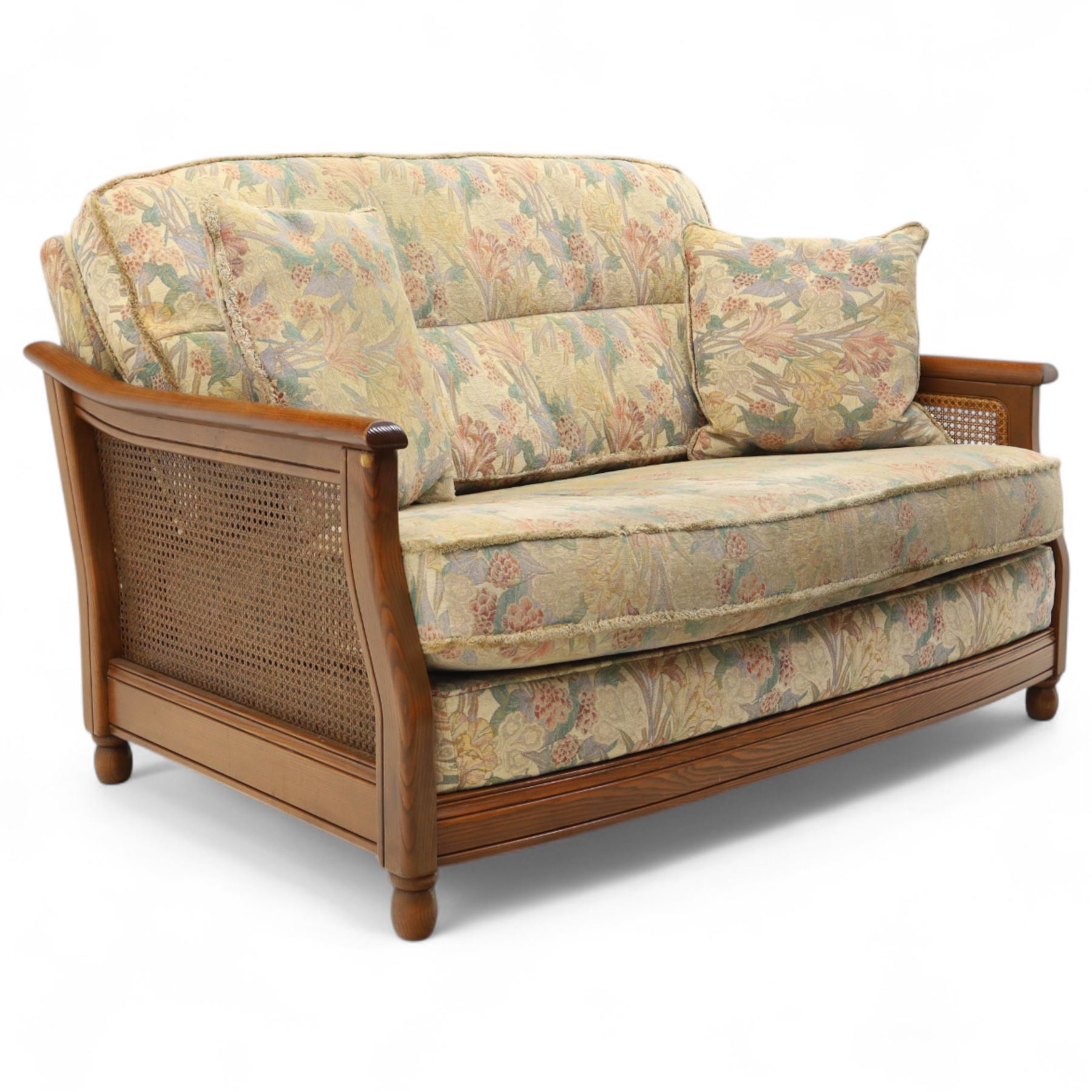 Ercol – bergère four piece suite, including armchair, two seat sofa, three seat sofa and footstool, all with removable floral upholstered cushions, the frames with side caning and rounded arm supports in stained beech

Three seat (H 87cm, D 89cm, W 196cm)
Two seat (H 87cm, D 89cm, W 137cm)
Armchair (H 87cm, D 89cm, W 87cm)
Footstool (H 28cm, D 55cm, W 55cm)
