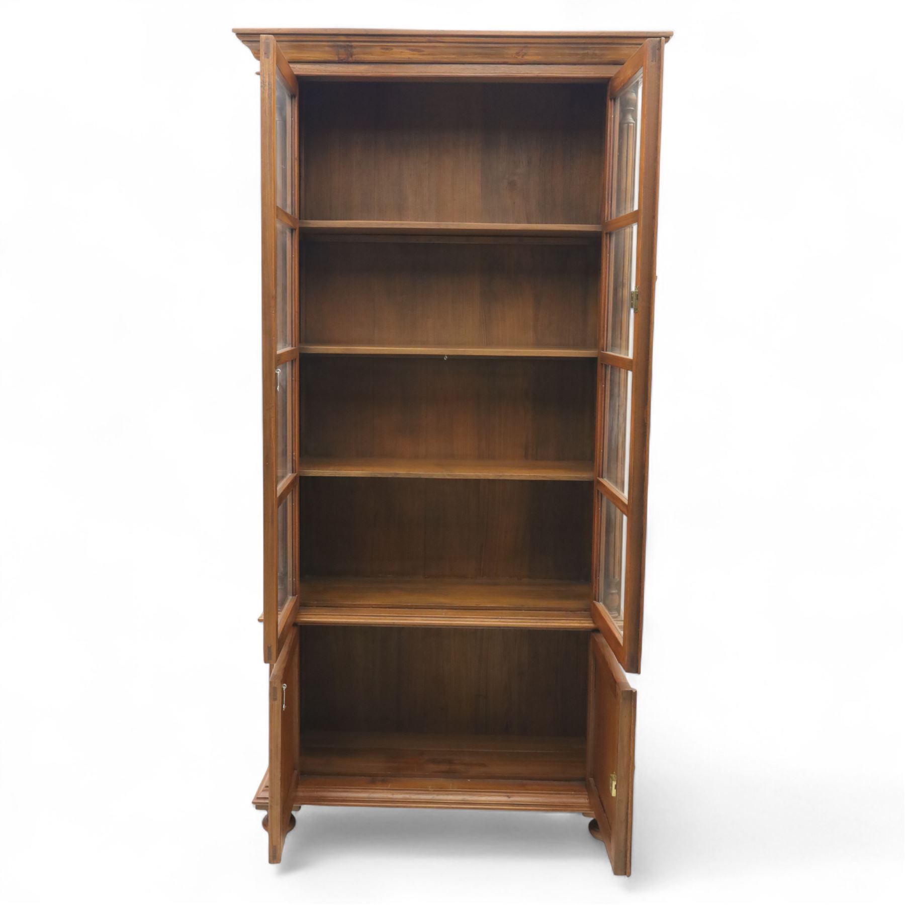 Pair of late 20th century Thai hardwood display cabinets, each with moulded cornice over twin glazed doors enclosing adjustable shelves, panelled cupboard doors below flanked by fluted columns, raised on bun feet