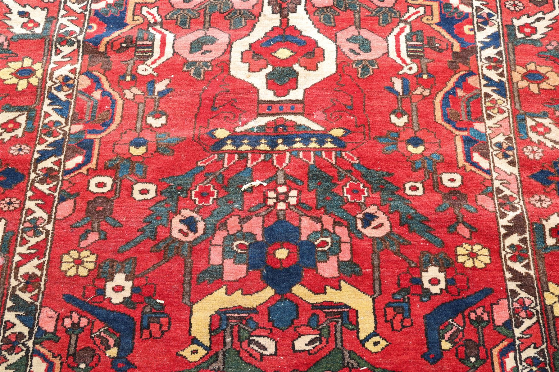 Vintage Persian Heriz crimson ground rug, the field decorated with a central stylised urn and bird of paradise motifs, the guard  lines with repeating stylised plant motifs of geometric form