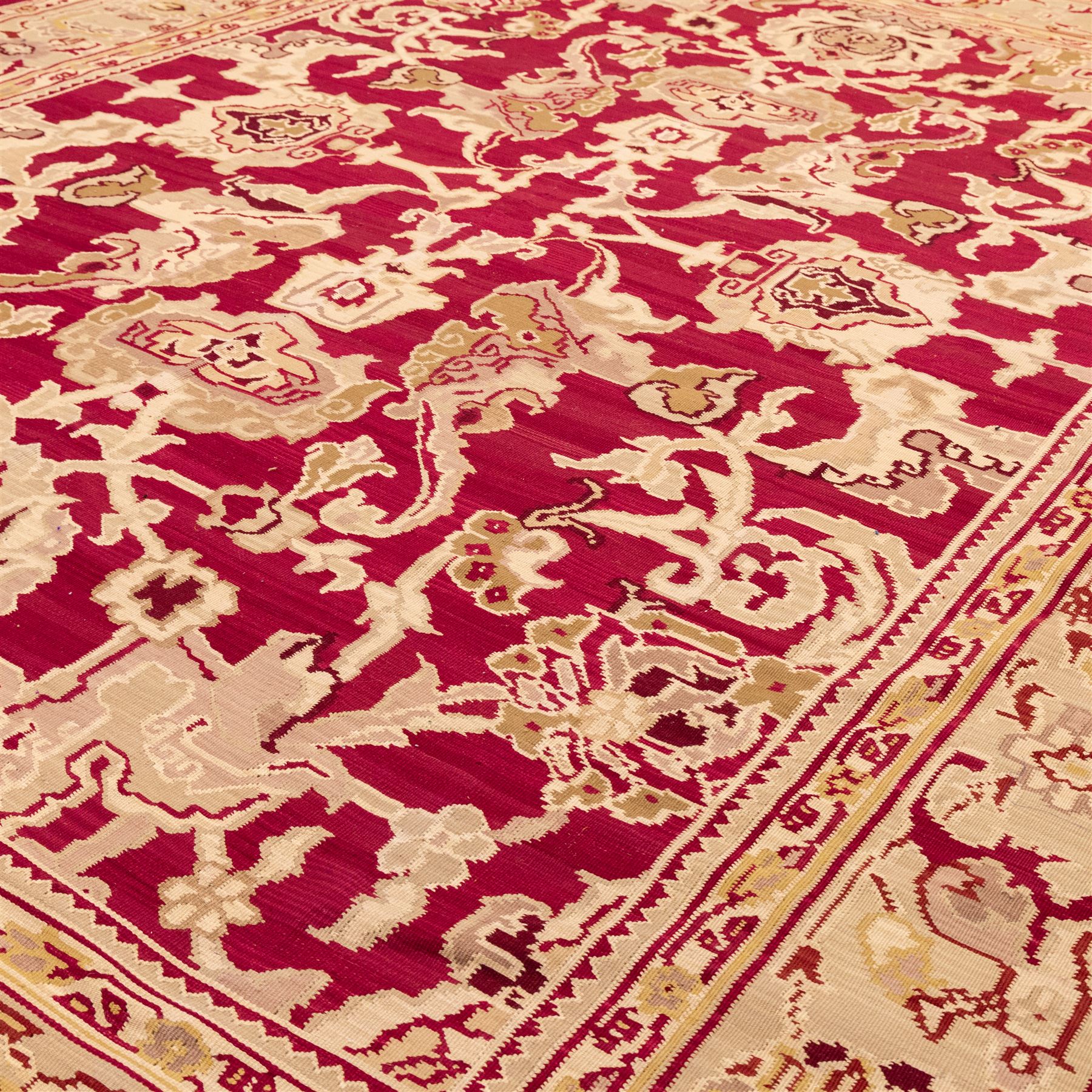 Large Persian Savonnerie-inspired style flatweave kilim, crimson field with central stylized palmette medallion with bold scrolling vinery and angular floral motifs between multiple guard stripes, rendered in tones of soft cream, pale sage, and muted terracotta, with fringe ends 