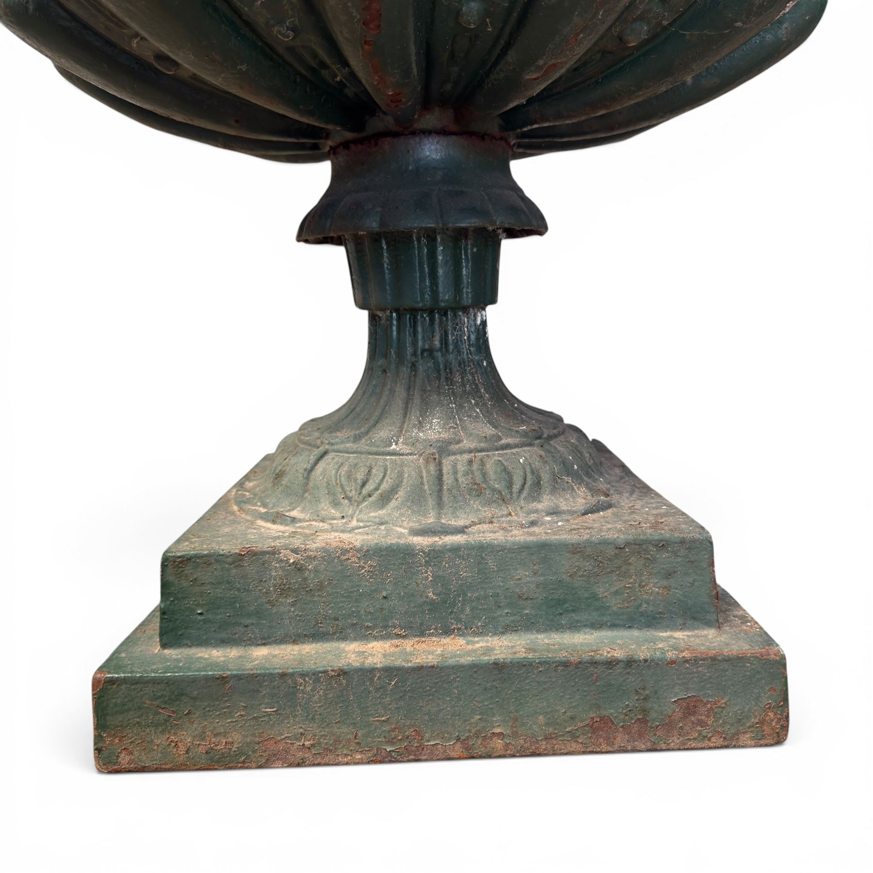 Pair of Victorian cast iron campana garden urns, the flared rim with repeating stylised anthemion motifs with scrollwork, over a deep gadrooned and Aesthetic moulded underbelly, fluted and foliate lower bowls on square pedestal bases, in antique green-painted finish
