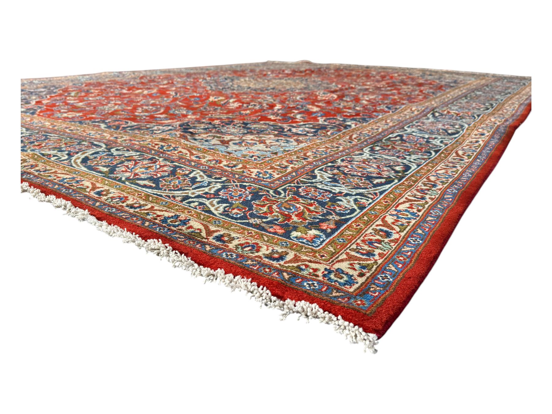 Central Persian Kashan carpet, the red field centred by a large multi-lobed floral medallion, flanked by corner spandrels in navy, enclosed by multiple scrolling floral borders, fringed to two ends