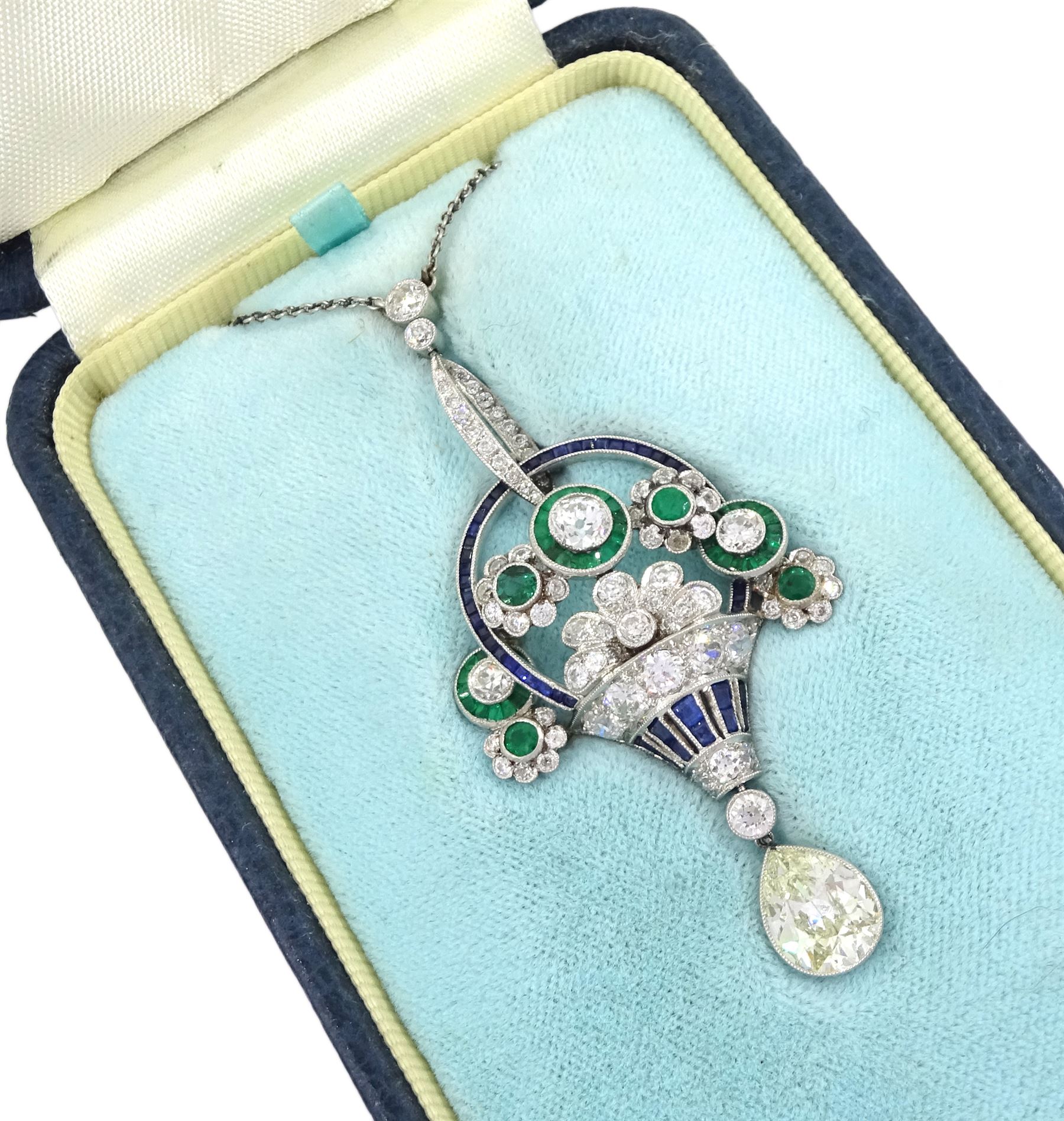 Art Deco platinum milgrain set diamond, emerald and sapphire flower basket pendant necklace, the basket set with old cut diamonds, calibre cut sapphires and emeralds, diamonds approx 2.00 carat, suspending a single pear cut diamond of approx 2.05 carat, on a platinum trace link chain necklace, stamped Plat, circa 1915-1920, in fitted box by Licht & Morrison, London