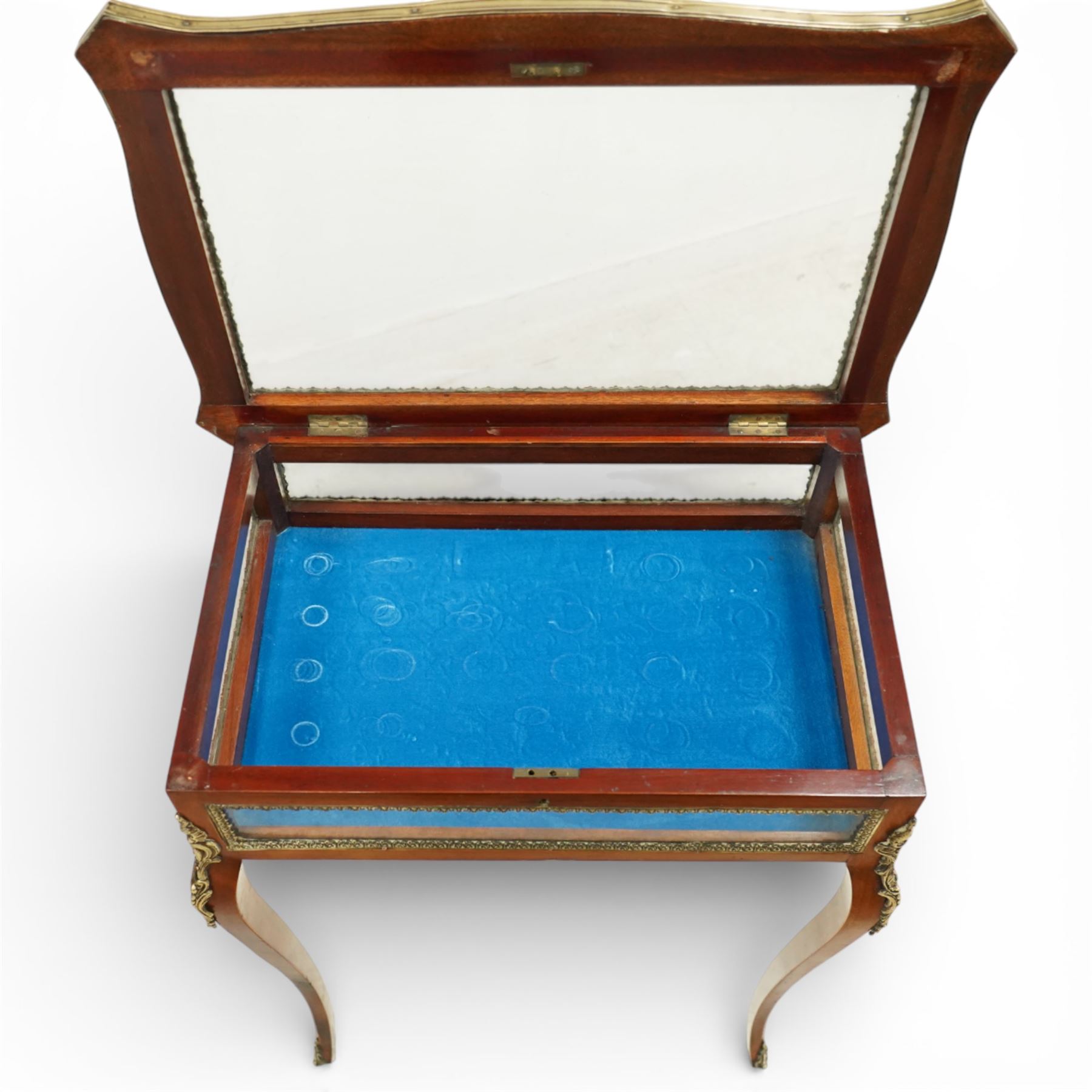 Early 20th century French mahogany bijouterie table, the hinged shaped rectangular top with brass edge and gilt-metal foliate slip enclosing bevelled glass plate, raised on cabriole supports with applied gilt-metal cartouche and foliate mounts
