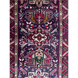 Northwestern Persian Heriz hand-knotted runner, dark indigo field with a series of linked stepped medallions in madder red, ivory, and green, flanked by angular floral motifs, within a madder red border of stylized rosettes and geometric vine motifs 405cm x 95cm