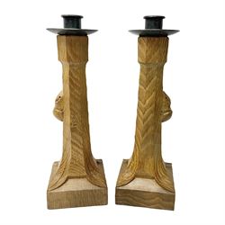 Mouseman - pair of tooled oak candlesticks, wrought iron sconce with drip tray over tapered octagonal column carved with mouse signature, terminating to stylised leaf carved square base, by the workshop of Robert Thompson, Kilburn
