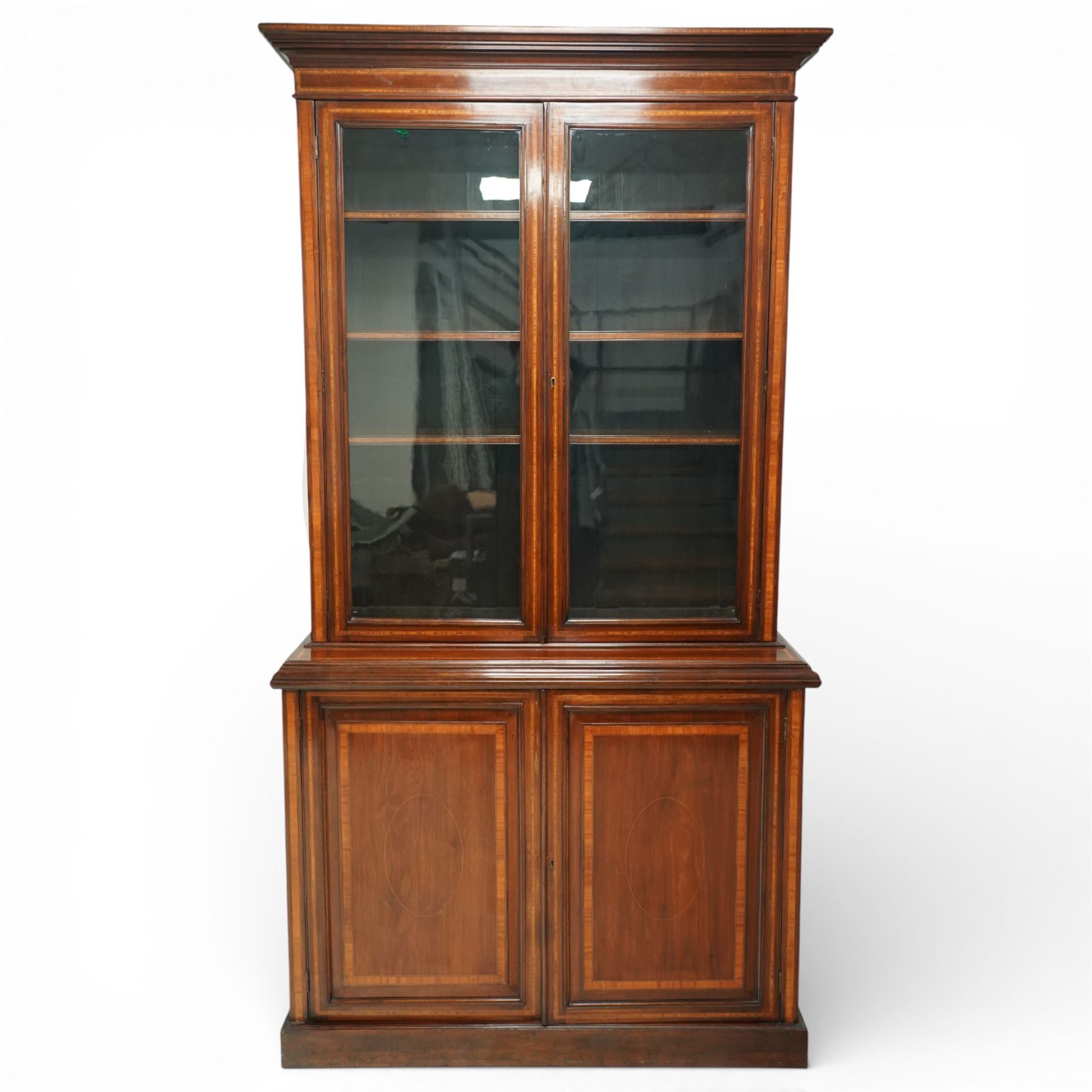 Large Edwardian walnut and satinwood enclosed bookcase-on-cupboard, projecting cornice over two glazed doors with satinwood and ebony banding and stringing enclosing three adjustable shelves, over two panelled doors enclosing two drawers above shelf, on skirted base