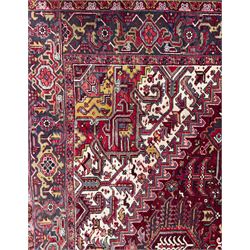 Northwestern Persian Heriz carpet, the madder red field centred by a large octofoil medallion with serrated edge, flanked by ivory stepped spandrels and geometric floral motifs in indigo, ochre and sky blue, enclosed by a navy border of rosettes and angular vines, from the region of Heriz
