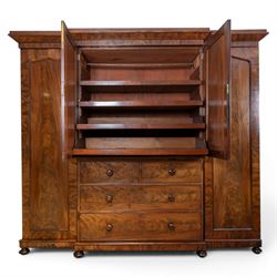 Early 19th century figured mahogany combination wardrobe, the breakfront architectural cornice over central press cupboard enclosing linen slides, flanked by full-height hanging cupboards with arched inset panels, lower arrangement of two short and two long drawers with turned knob handles, applied acanthus carved detail, raised on bun feet
