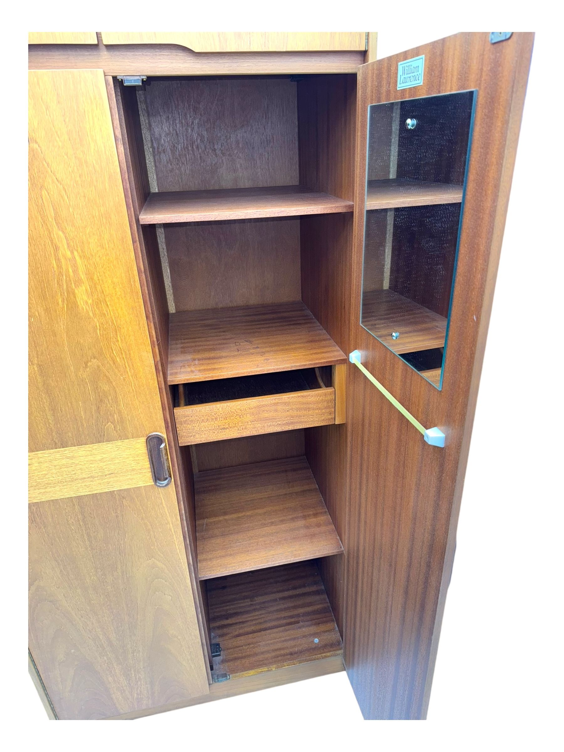 William Lawrence - mid-20th century teak double wardrobe, upper storage section over twin doors featuring recessed handles and contrasting horizontal panel, enclosing hanging rail compartment, towel rail, mirror, shelves and drawer, on plinth base with concealed castors