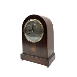 Edwardian - German 8-day mahogany mantle clock with a round top and satinwood inlay to the front, on a shallow base raised on button feet, silvered dial with arabic numerals and spade hands, cast brass bezel with a convex glass, rack striking twin train movement, sounding the hours and half hours on a coiled gong. With pendulum. 