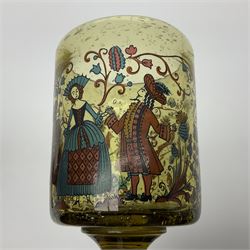 19th Century Bohemian amethyst glass lidded goblet, the bowl of faceted form, gilded with three children in period dress playing games, upon a knopped stem and conforming faceted foot, together with an art nouveau green glass goblet, with gilded rim, upon clear trumpet stem, and a hand blown wine glass, transfer printed with birds and three figures in period dress, tallest H29cm