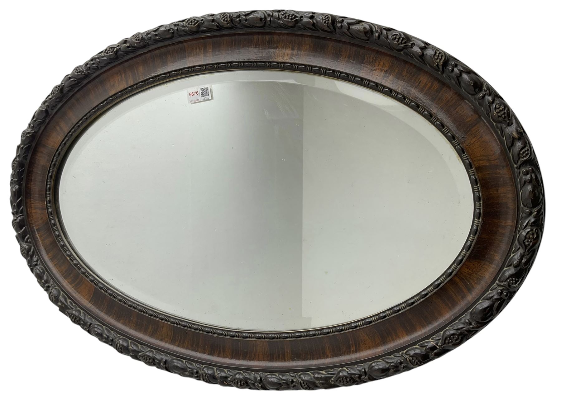Early 20th century oval mirror, moulded frame decorated with trailing foliage and berries, bevelled plate