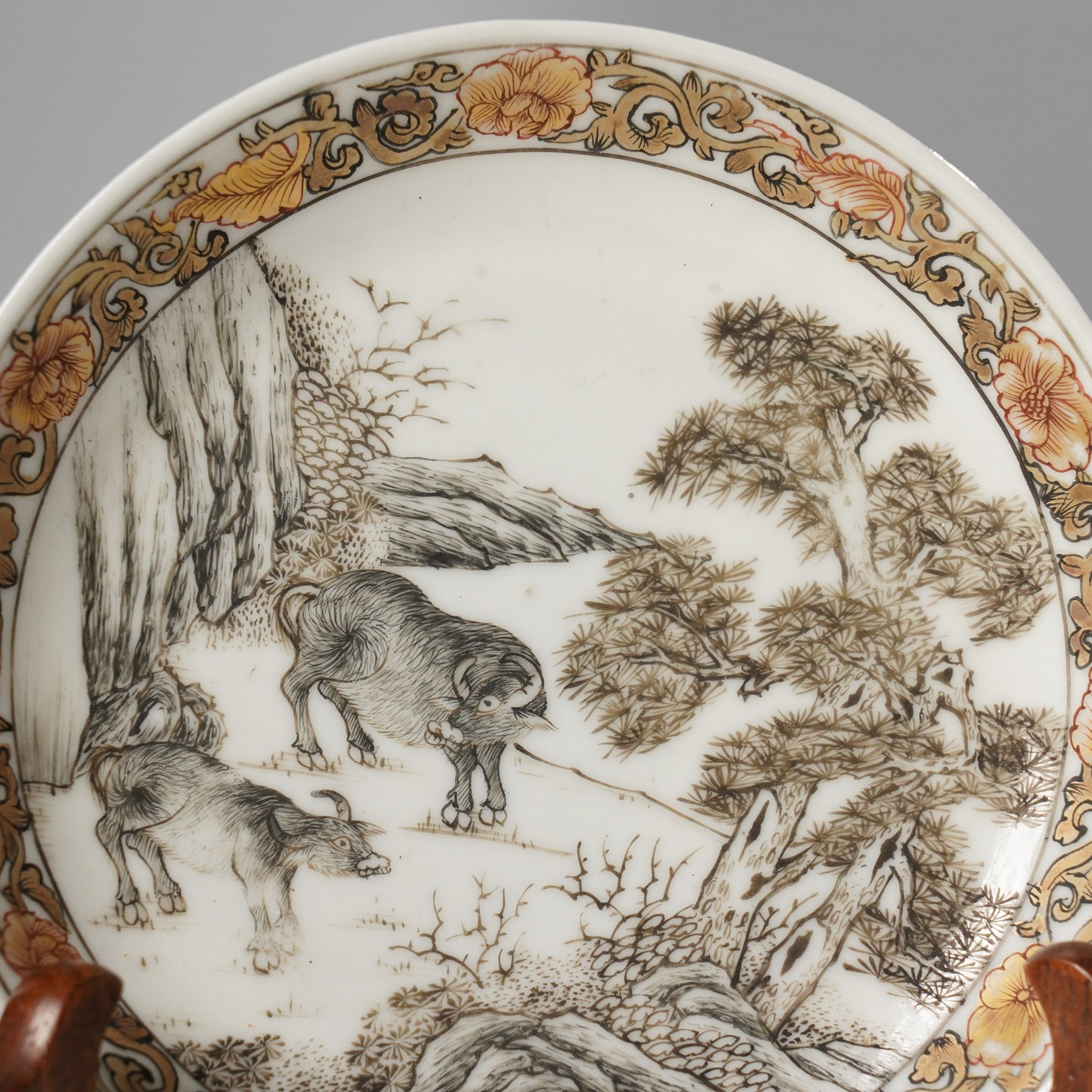 Chinese Yongzheng period saucer, finely painted in grisaille with buffalo within a rocky landscape, the inner rim with iron red and gilt foliate band, D11.5cm