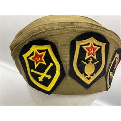 Four side caps - WW2 Russian, post-WW2 Russian and two East German; all with badges, one with multiple metal badges (4)