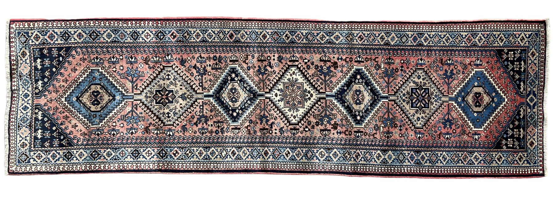 Persian Yalameh coral ground runner rug, the field decorated with seven hooked lozenge medallions surrounded by stylised plant motifs, the indigo spandrels decorated with similar patterns, guarded border with repeating diamond lozenges