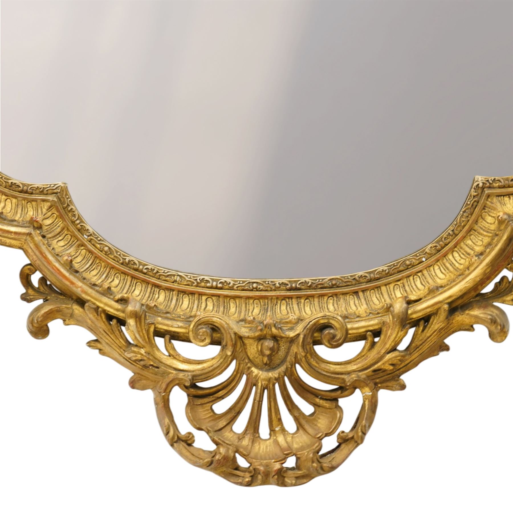 Victorian giltwood and gesso framed ornate wall mirror, the protruding cartouche pediment decorated with extending scrolls of acanthi and flower heads, with scrolled foliage corners flanking a carved slip with further gadrooned scroll decoration, contained a shaped rectangular bevelled plate, over a pierced and scrolling scallop shell terminal