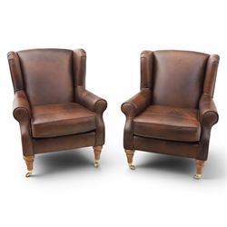 Marks & Spencer - Pair of brown leather wing back chairs, raised on light stained supports...