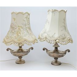 A pair of silver plated table lamps, of urn form with twin scroll handles and acanthus detail, raised upon circular feet, with floral tasselled shades, overall H63cm. 