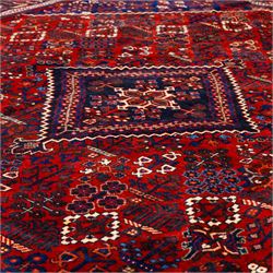 Central Persian Joshagen hand-knotted carpet, madder-red field with a central stepped lozenge medallion and densely filled with stylized geometric floral and tree motifs arranged in a repeating lattice enclosed by indigo spandrels and a broad navy border of angular palmette and vine ornament, flanked by multiple guard stripes, cotton fringe ends 